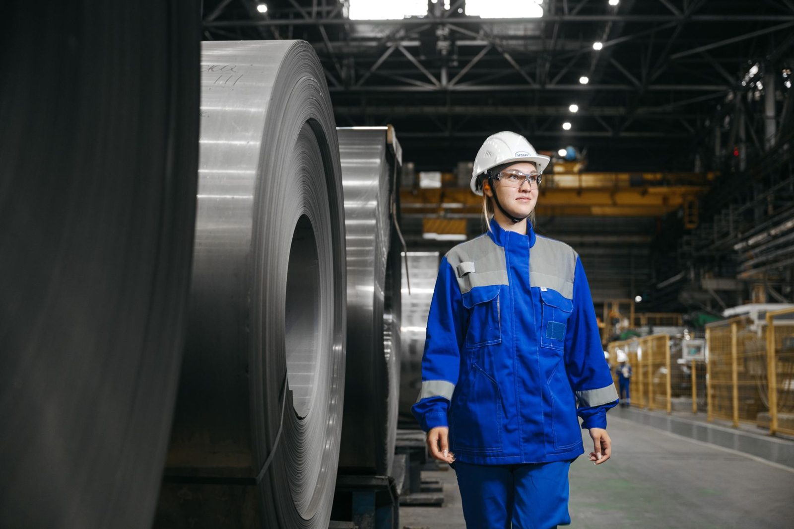 A plant worker in a hard hat walking past steel coils