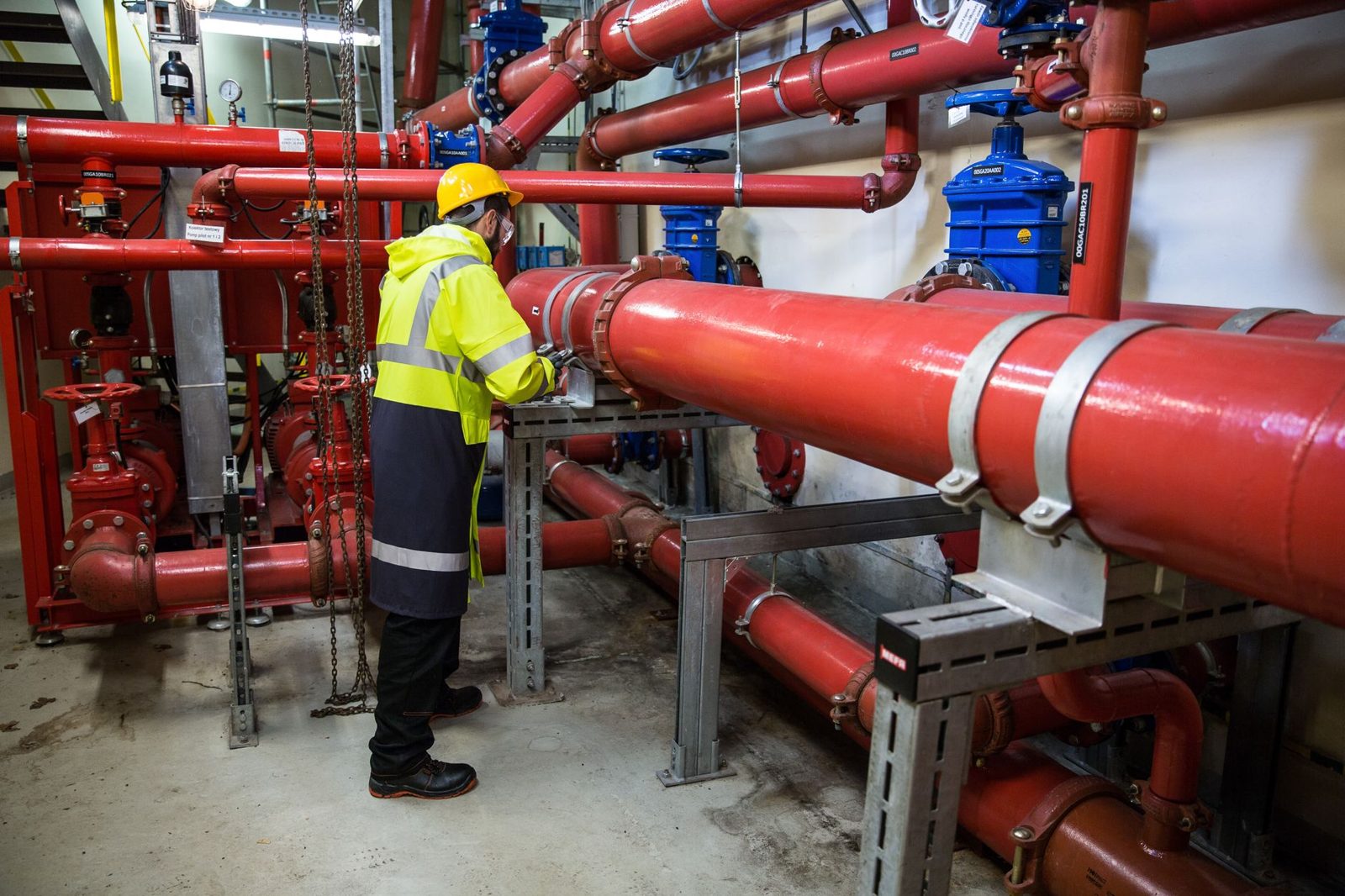 A worker in a hard hat among red pipes in a plant