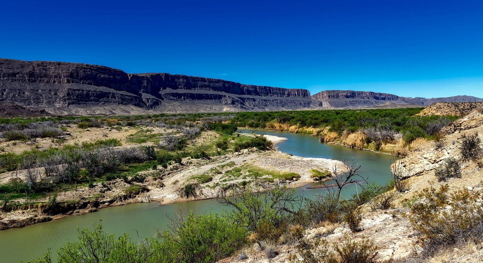 The Rio Grande winding between brush and cliffs on the Texas border
