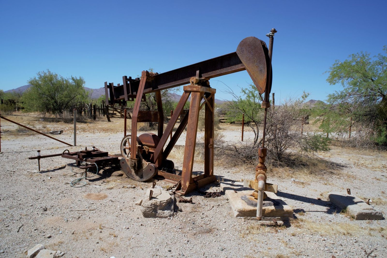 A pumpjack and storage tanks on a dusty lease road in the Permian Basin