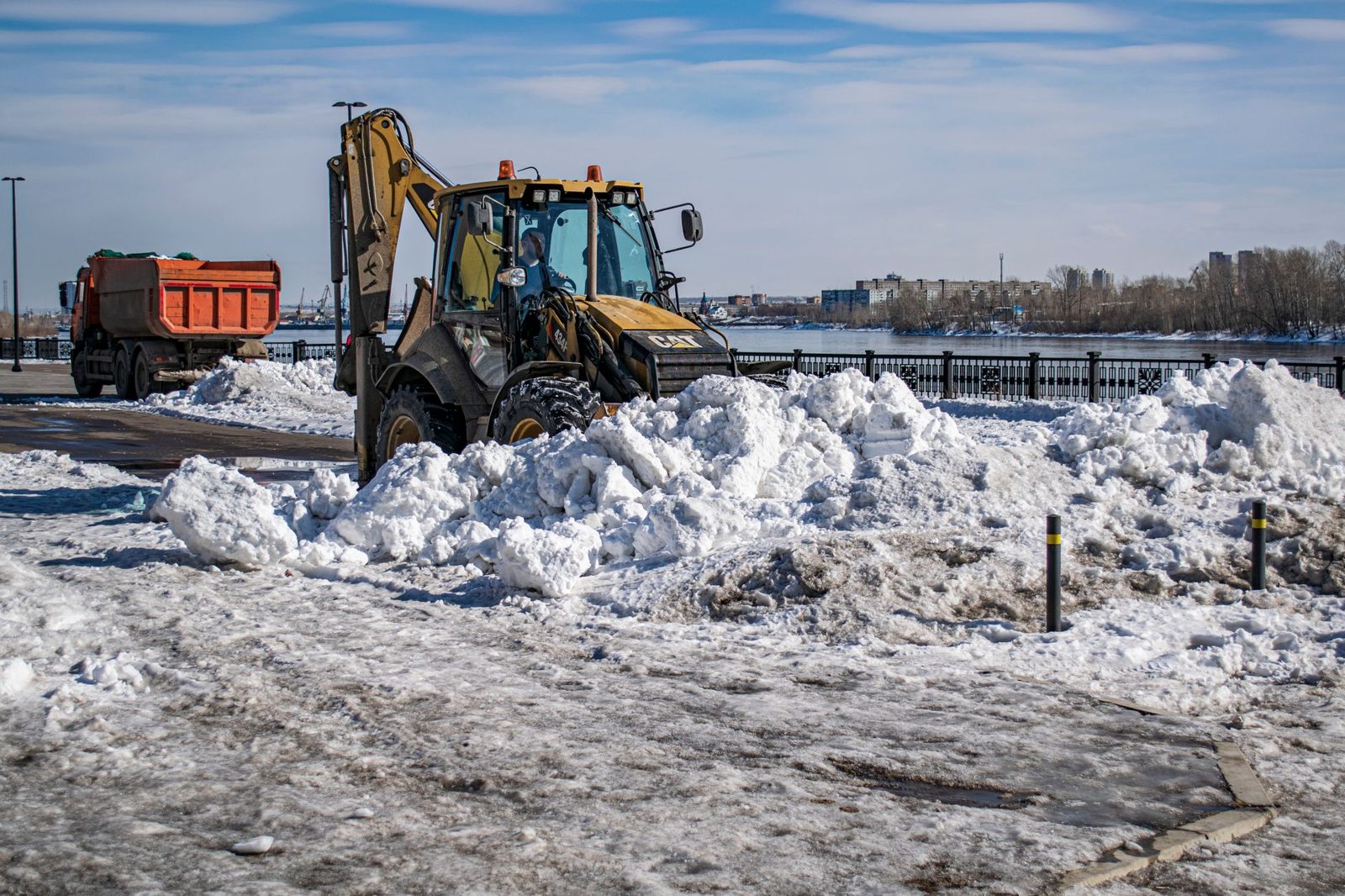 Snow piled around a work site with trucks and a loader