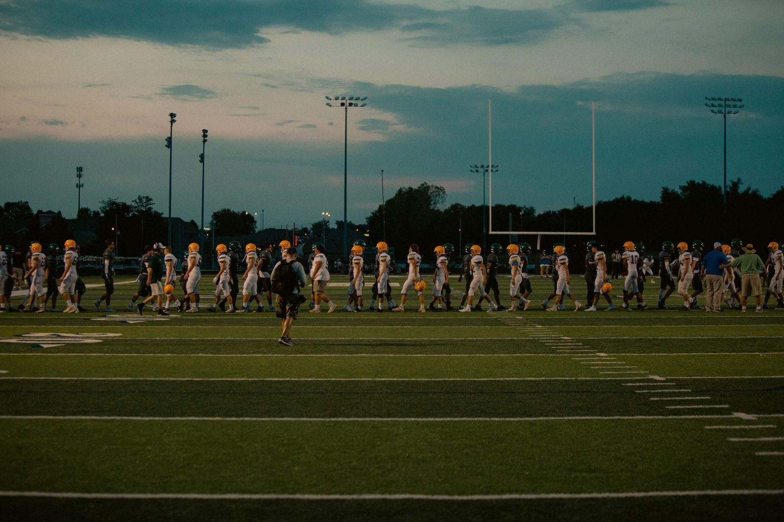 A football team practicing on a field at dusk
