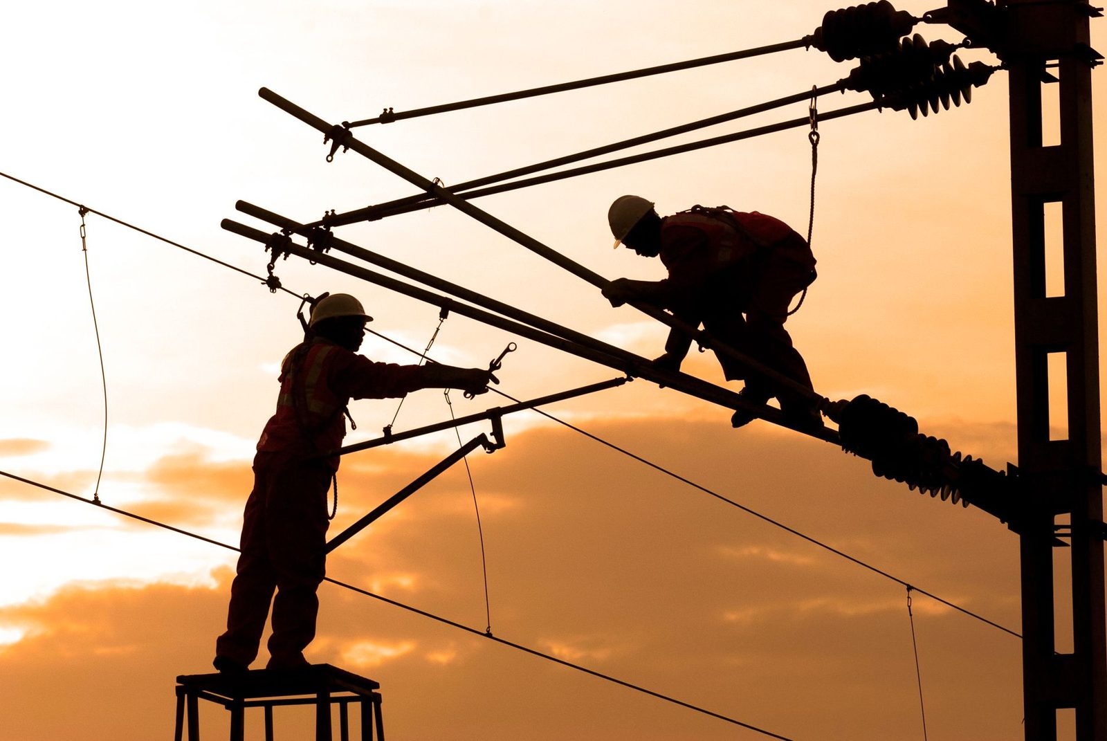 Line workers silhouetted on a pole at sunset
