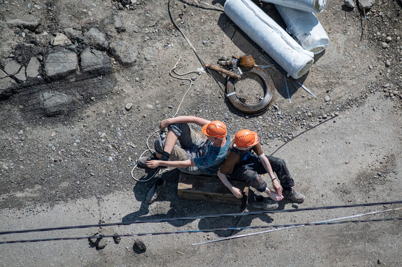 Two workers in hard hats sitting down for a break among equipment on a dusty job site