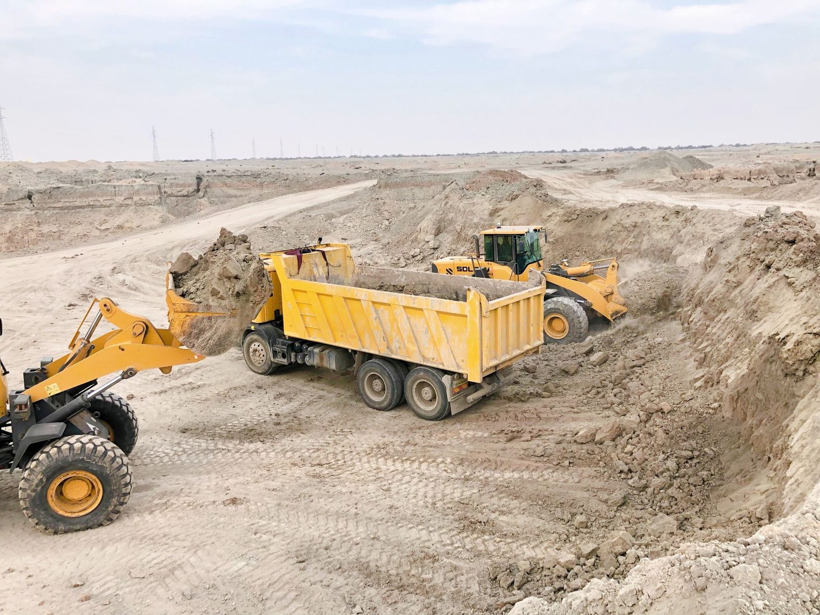 A wheel loader filling a dump truck during earthwork on a large, dusty construction site