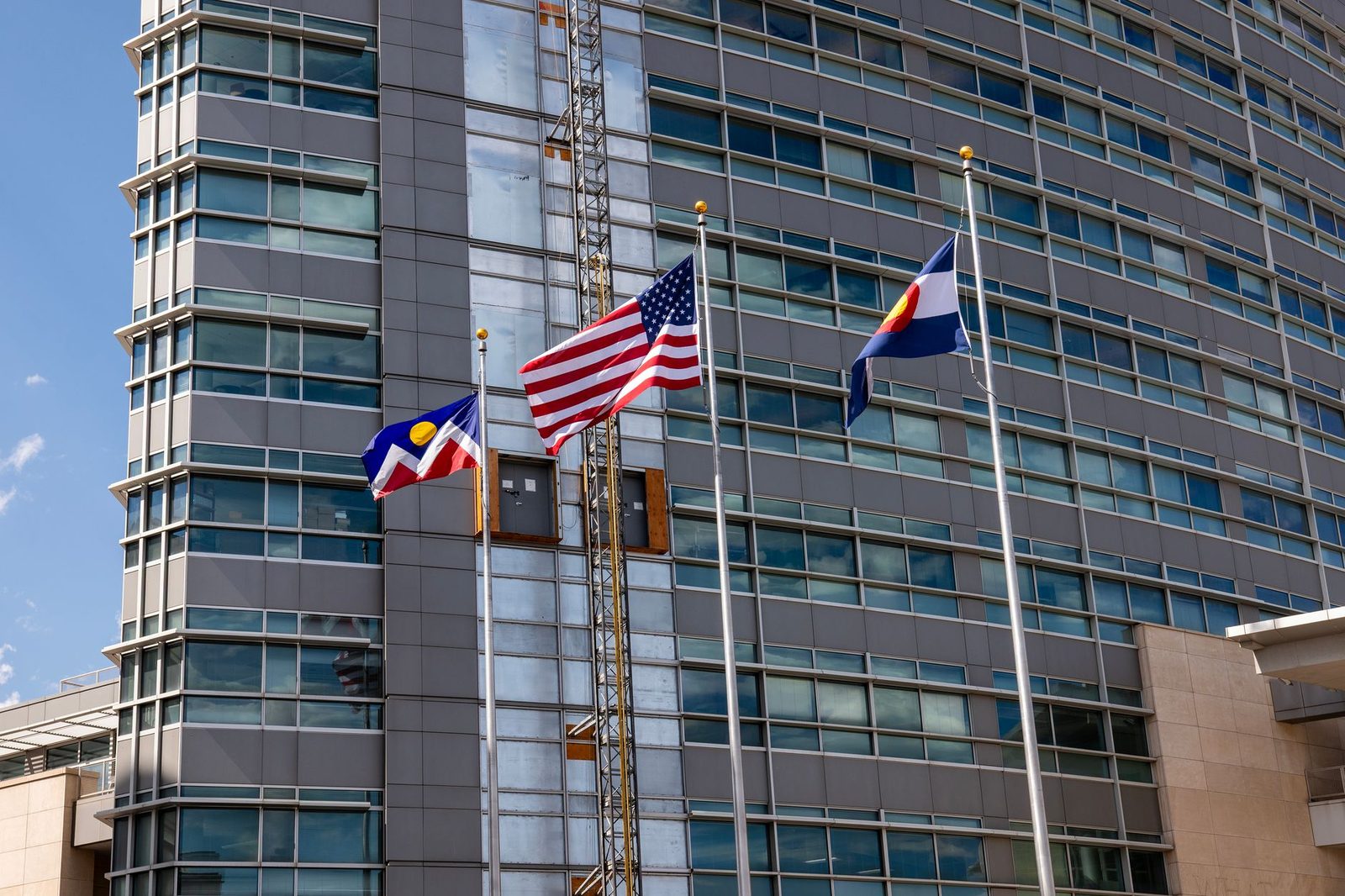 A tower crane beside a Denver building flying the Colorado and Denver flags