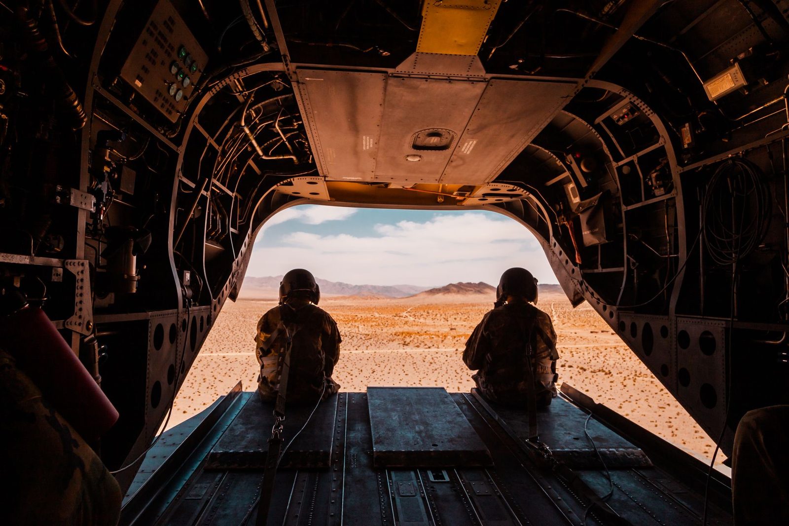 Soldiers looking out the open rear ramp of a military helicopter over desert terrain