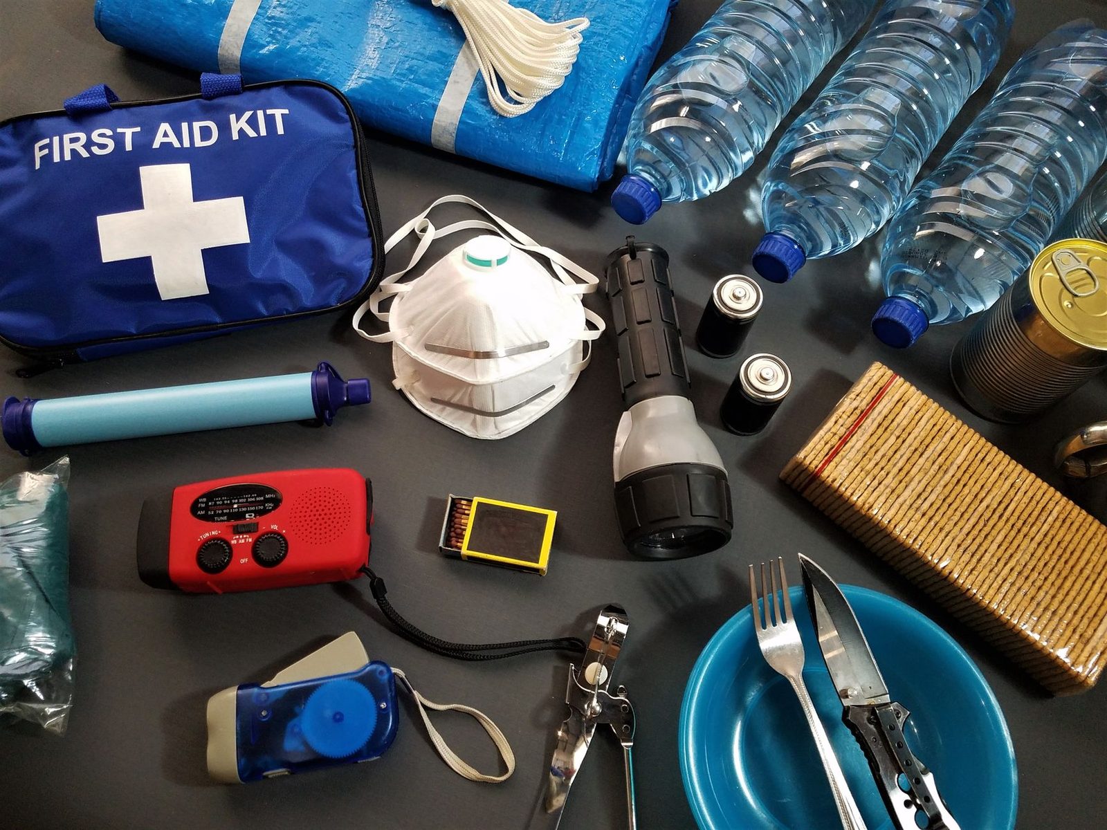 An emergency kit laid out with bottled water, a first aid kit, a dust mask and a flashlight