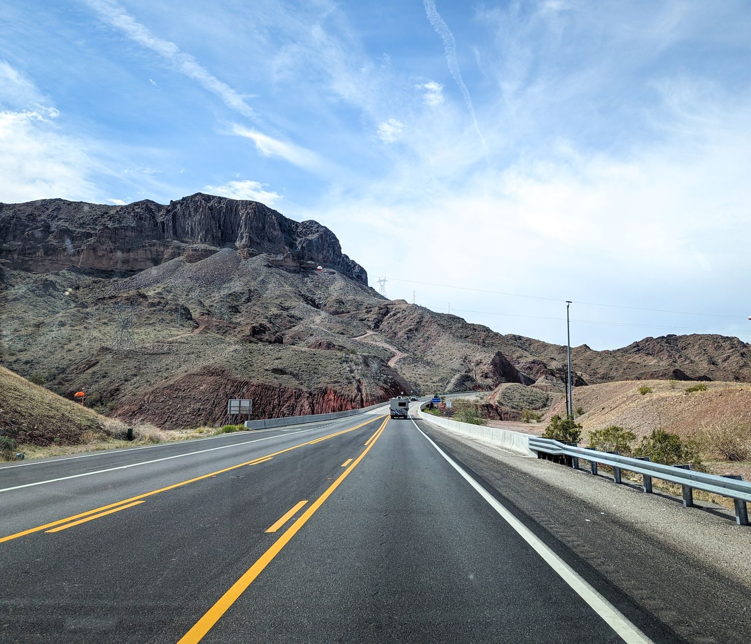 A divided desert highway winding through dry, rocky Mojave mountains under a hot summer sky