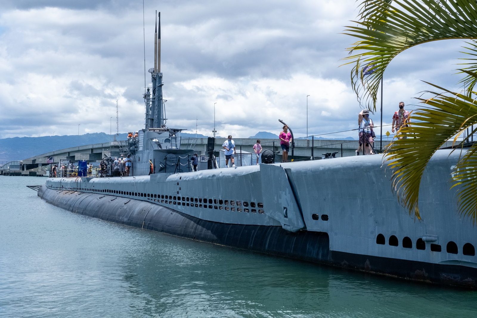 A submarine museum ship moored at Pearl Harbor with the Oahu ridges behind