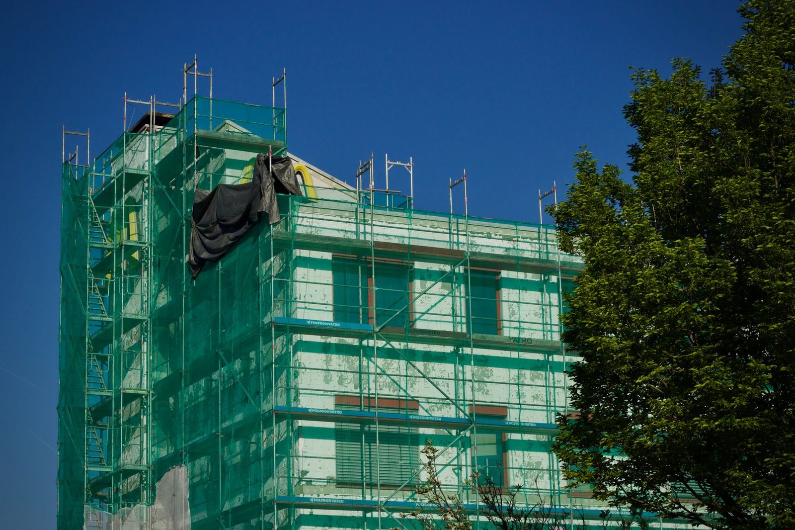 A building wrapped in scaffolding and safety netting during a summer renovation
