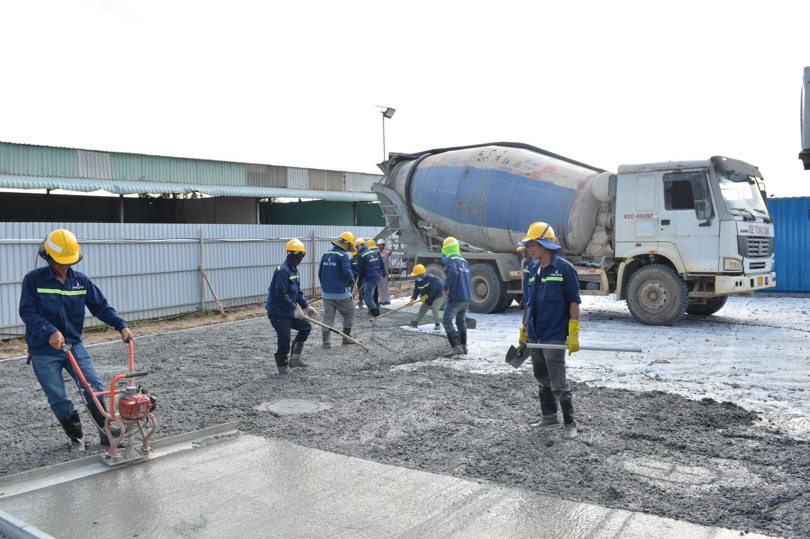 A construction crew pouring and finishing a concrete slab next to a ready-mix truck