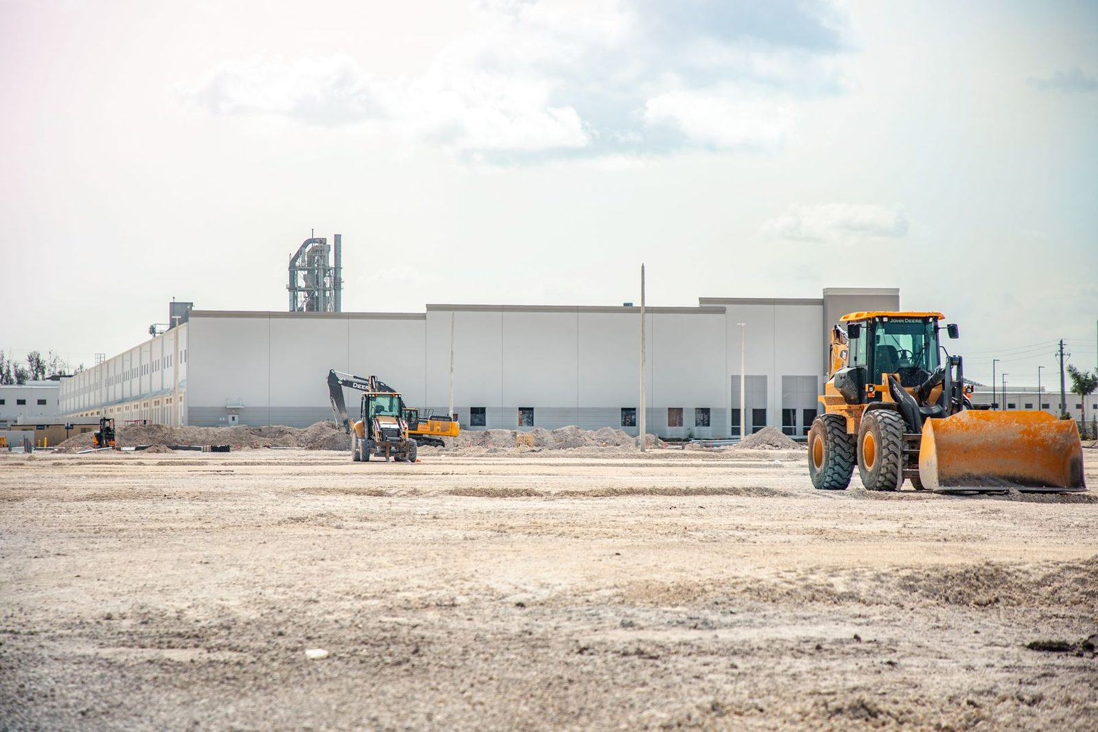 A large warehouse construction site with a loader working the graded pad under a clear summer sky