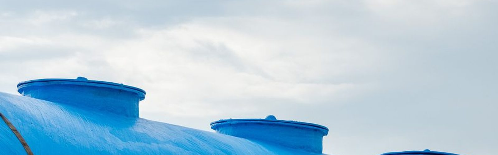 The top of a large blue water storage tank against a cloudy sky