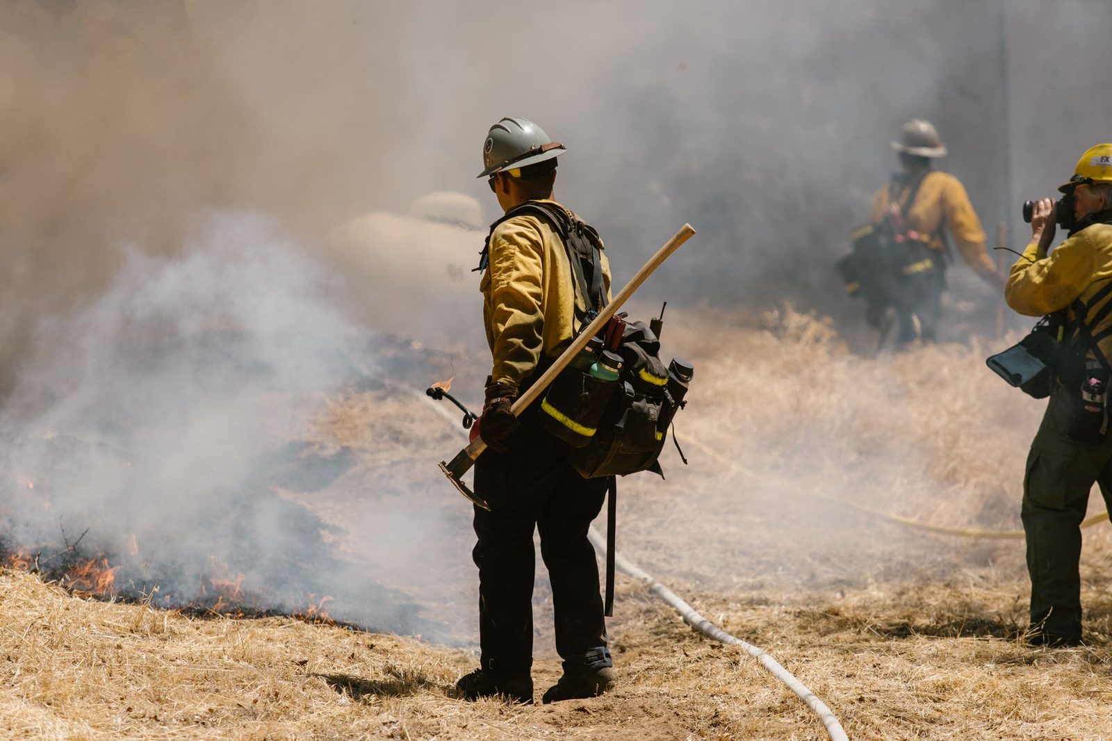 A wildland fire crew working a smoky grass fire in dry hills